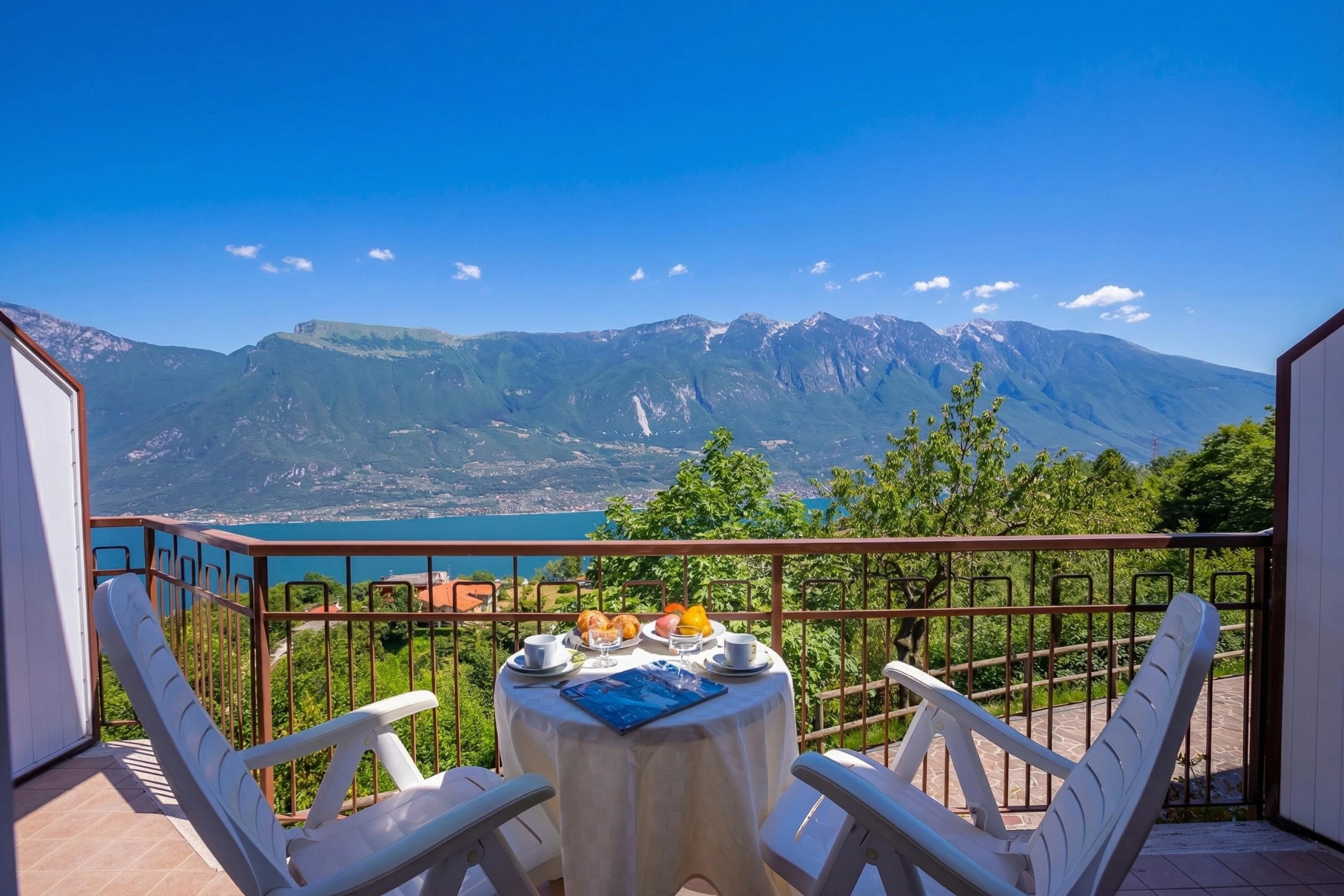A balcony with a table set for breakfast, overlooking a mountainous landscape and a body of water.