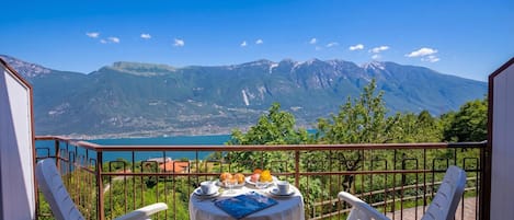 A balcony with a table set for breakfast, overlooking a mountainous landscape and a body of water.