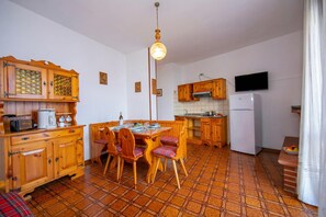 Una cucina compatta con mobili in legno, un tavolo da pranzo con sedie, un frigorifero e un televisore montato a parete.