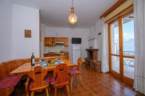 Cucina con mobili in legno, un tavolo da pranzo con sedie, un lampadario a sospensione, un frigorifero e vista attraverso un'ampia finestra.