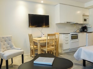 A modern kitchen with white cabinets, a flat-screen TV mounted above the counter, and a dining area with a table and chairs.