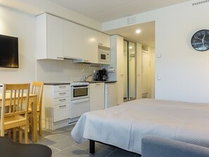 A compact room with a bed, a kitchenette, a dining area, and a clock on the wall.