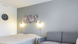 A modern hotel room with a bed, a gray sofa, a small table, and a wall clock. - Skistar 105 by Interhome (Kittilä)