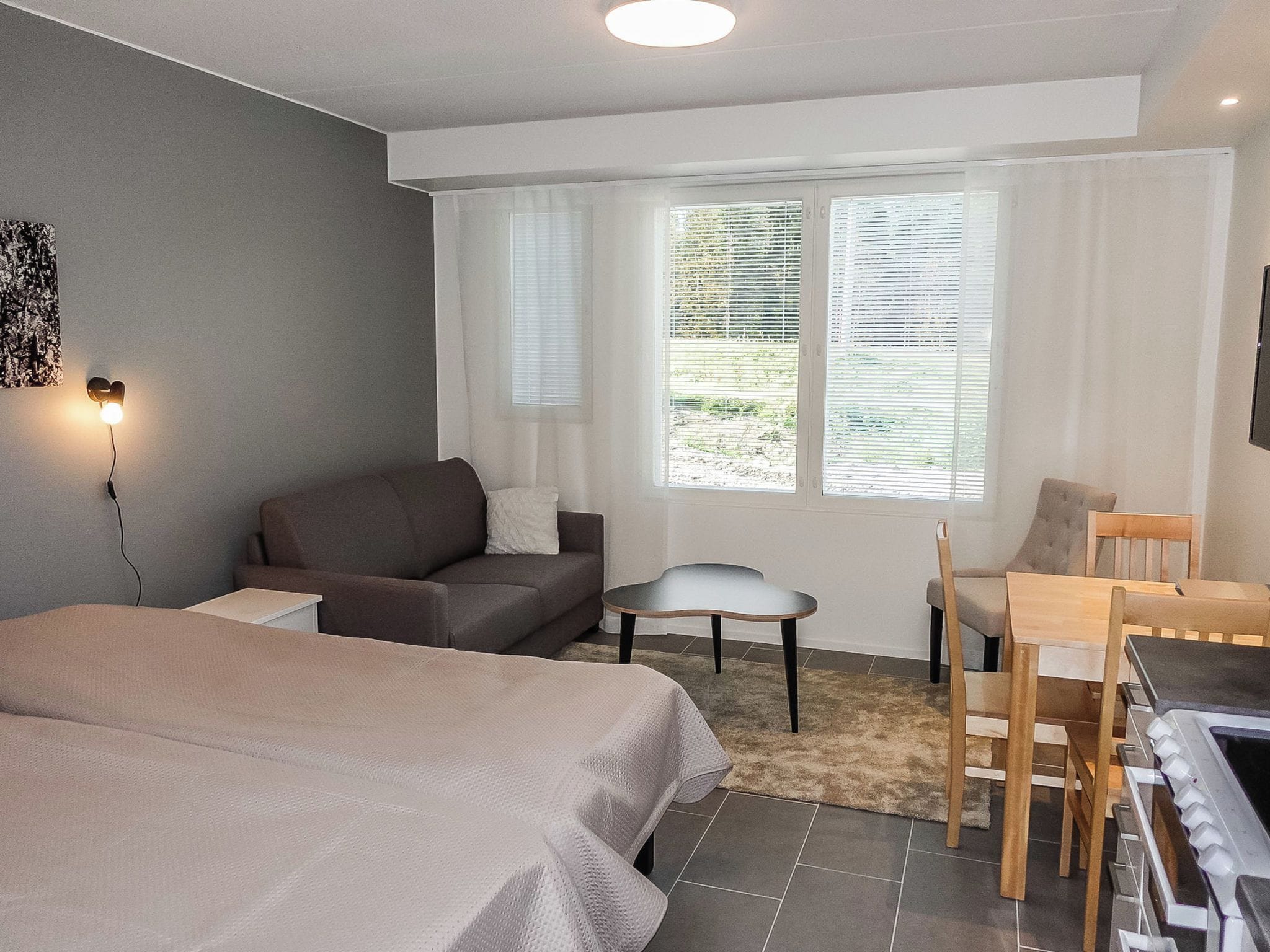 A hotel room with a bed, a sofa, a desk with a chair, and a window with blinds.