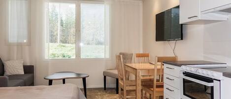 Habitación de hotel compacta con una cama, una mesita, una silla, un televisor montado en la pared y una kitchenette con horno.