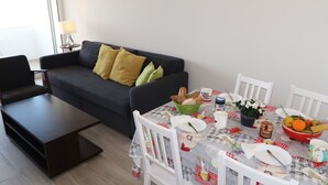 Uma sala de estar moderna com um sofá cinza escuro, uma mesa de centro e uma mesa de jantar posta com pratos, tigelas e uma cesta de pão.