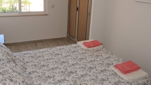Quarto com cama, janela com vista para a praia, guarda-roupa e um quadro na parede.