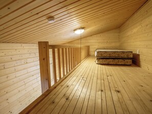 A wooden attic room with a sloped ceiling, a wooden railing, and a mattress on the floor.