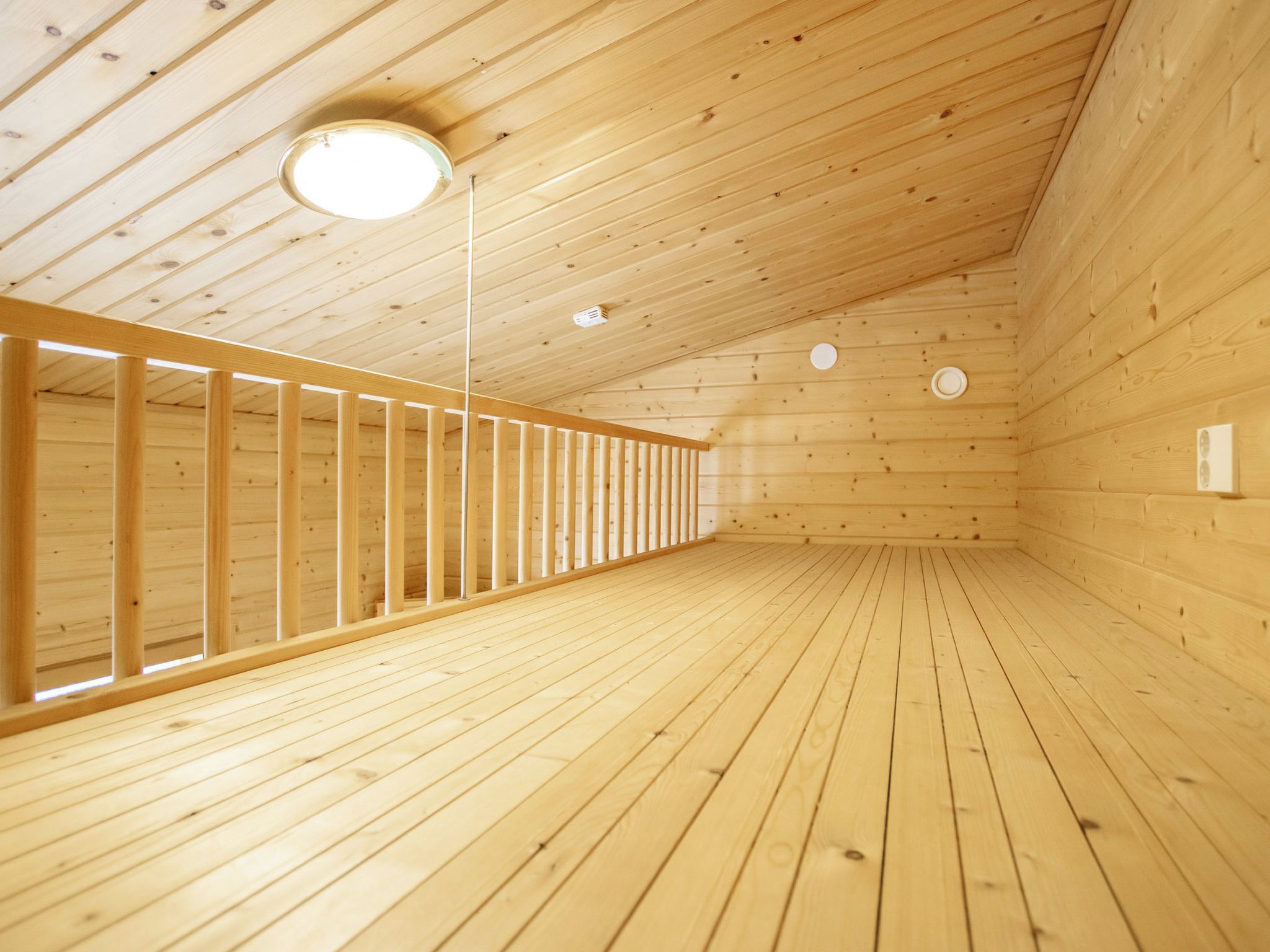 Ein Holzinnenraum mit schrägverlaufender Decke, einer zentralen Leuchte und einem langen, schmalen Raum mit Holzwänden und Holzboden.