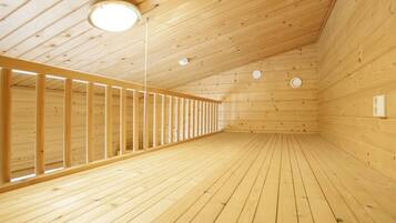 Ein Holzinnenraum mit schrägverlaufender Decke, einer zentralen Leuchte und einem langen, schmalen Raum mit Holzwänden und Holzboden.