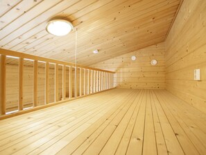 A wooden interior with a sloped ceiling, a central light fixture, and a long, narrow room with wooden walls and floor.