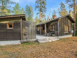 A cabin with a wooden exterior, a porch with a table and chairs, and a view of the surrounding forest.