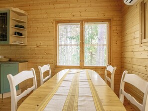 A wooden-paneled room with a long dining table, white chairs, a small kitchenette, and a window with blinds.