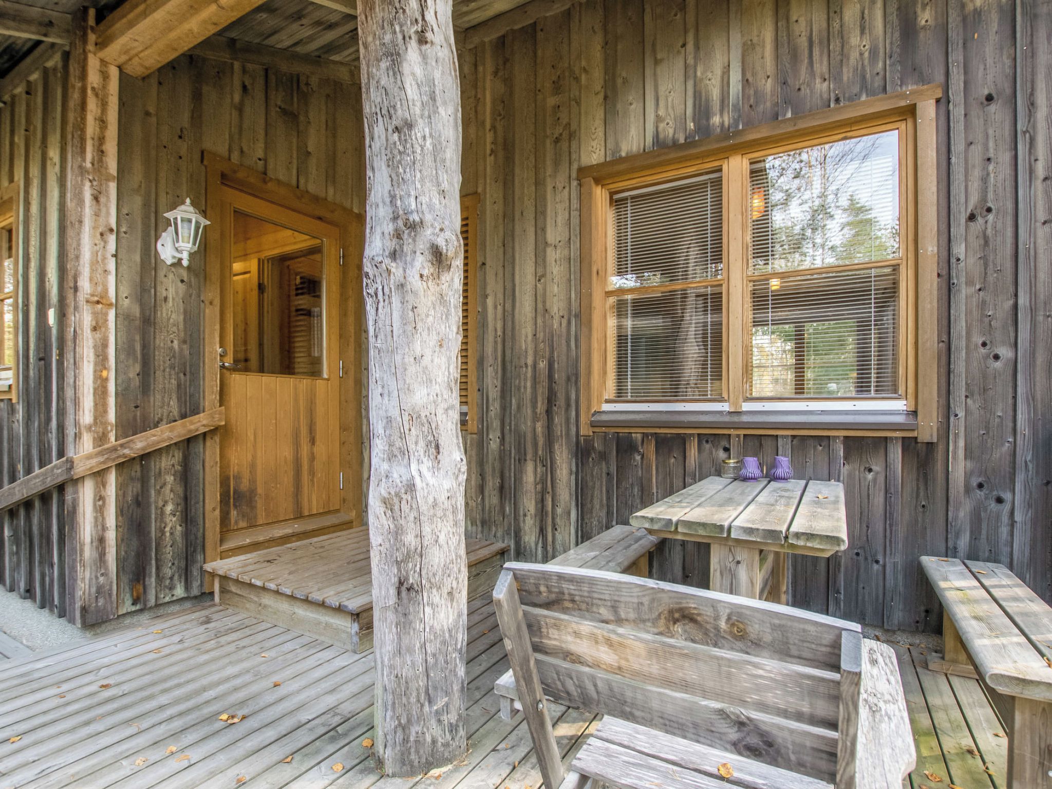 Eine Holzhütte mit Veranda, einer Bank und einem Tisch mit zwei violetten Vasen.