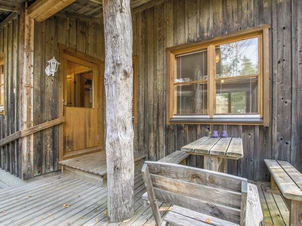 A wooden cabin with a porch, a bench, and a table with two purple vases.
