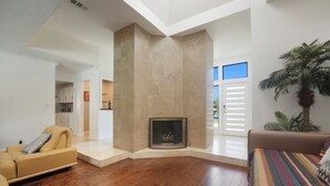 A spacious living room with a fireplace, wooden flooring, and a large window.