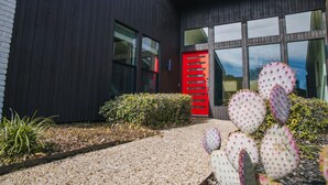 A modern building with a dark facade, a red door, and a cactus in the foreground.
