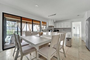 Une cuisine moderne avec des meubles blancs, un coin repas comprenant une table et des chaises, et une vue dégagée grâce à de grandes fenêtres.
