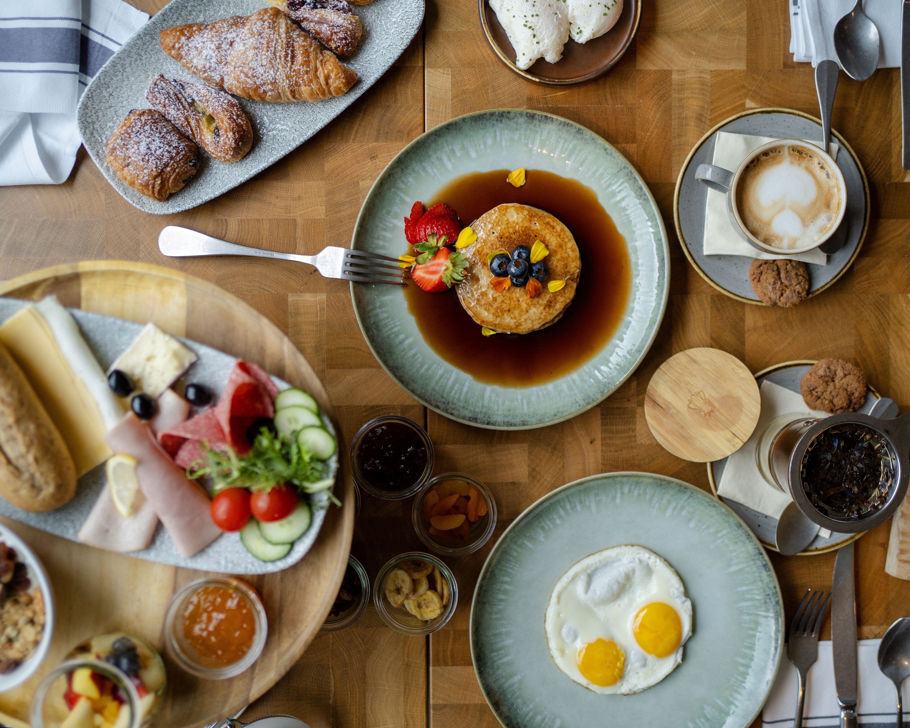 Una mesa de madera con diversos platos, incluyendo panqueques, huevos y pasteles.
