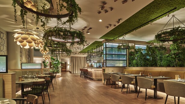 A restaurant with wooden flooring, hanging plants, and a bar area. - voco The Hague by IHG (The Hague)