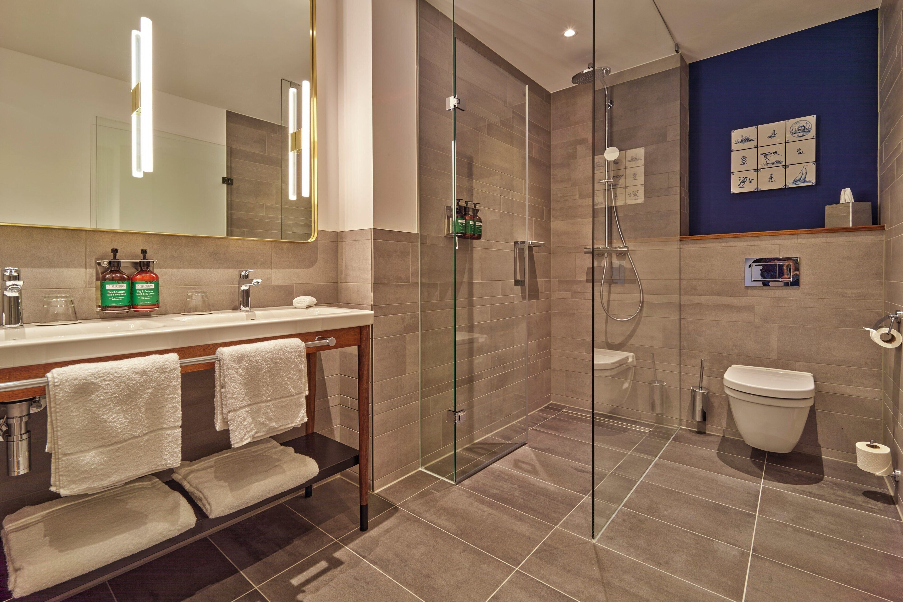 A modern bathroom with a glass-enclosed shower, a white toilet, and a vanity with a mirror and two bottles of shampoo.