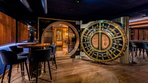A bar area with a large, ornate vault door, a round table with chairs, and a wooden wall. - voco The Hague by IHG (The Hague)