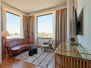 A modern hotel room with a leather sofa, a glass dining table, a telescope, and large windows offering a city view. - voco The Hague by IHG (The Hague)