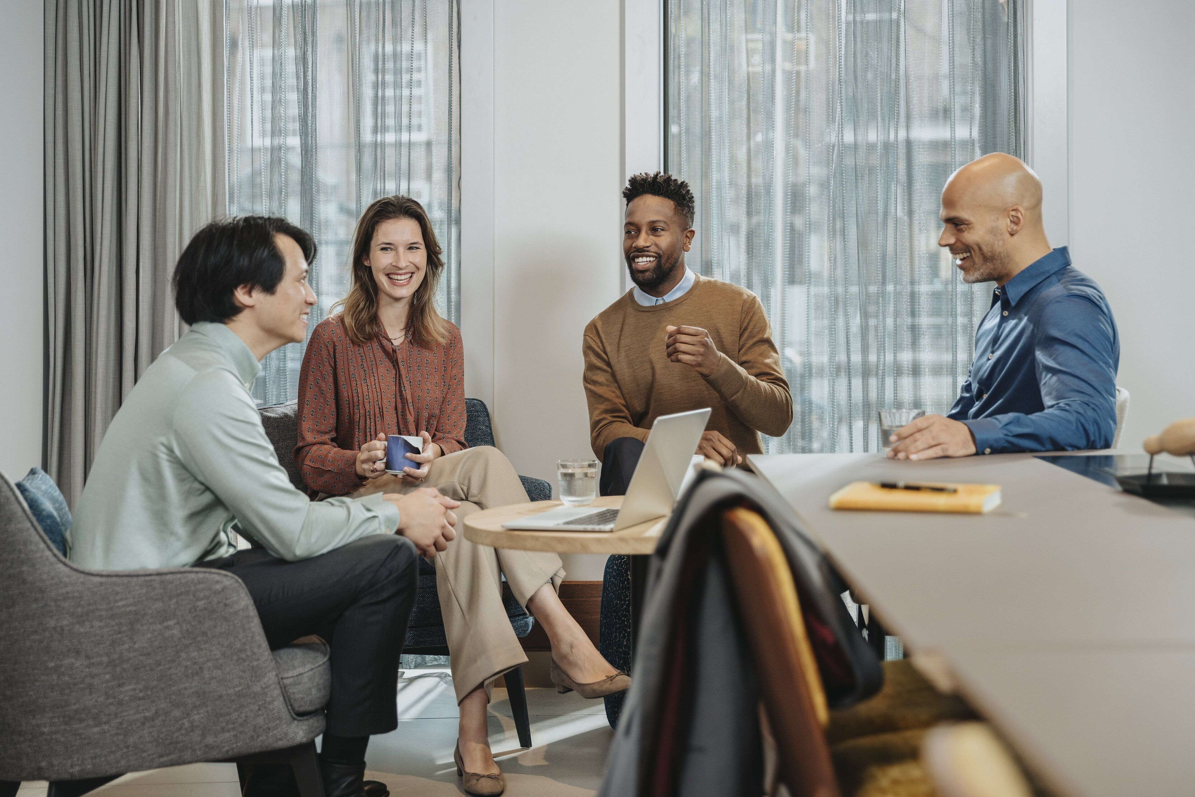 A group of people in a meeting room with a round table, chairs, and a laptop.
