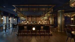 A bar area with a central bar, seating, and a decorative pillar. - voco The Hague by IHG (The Hague)