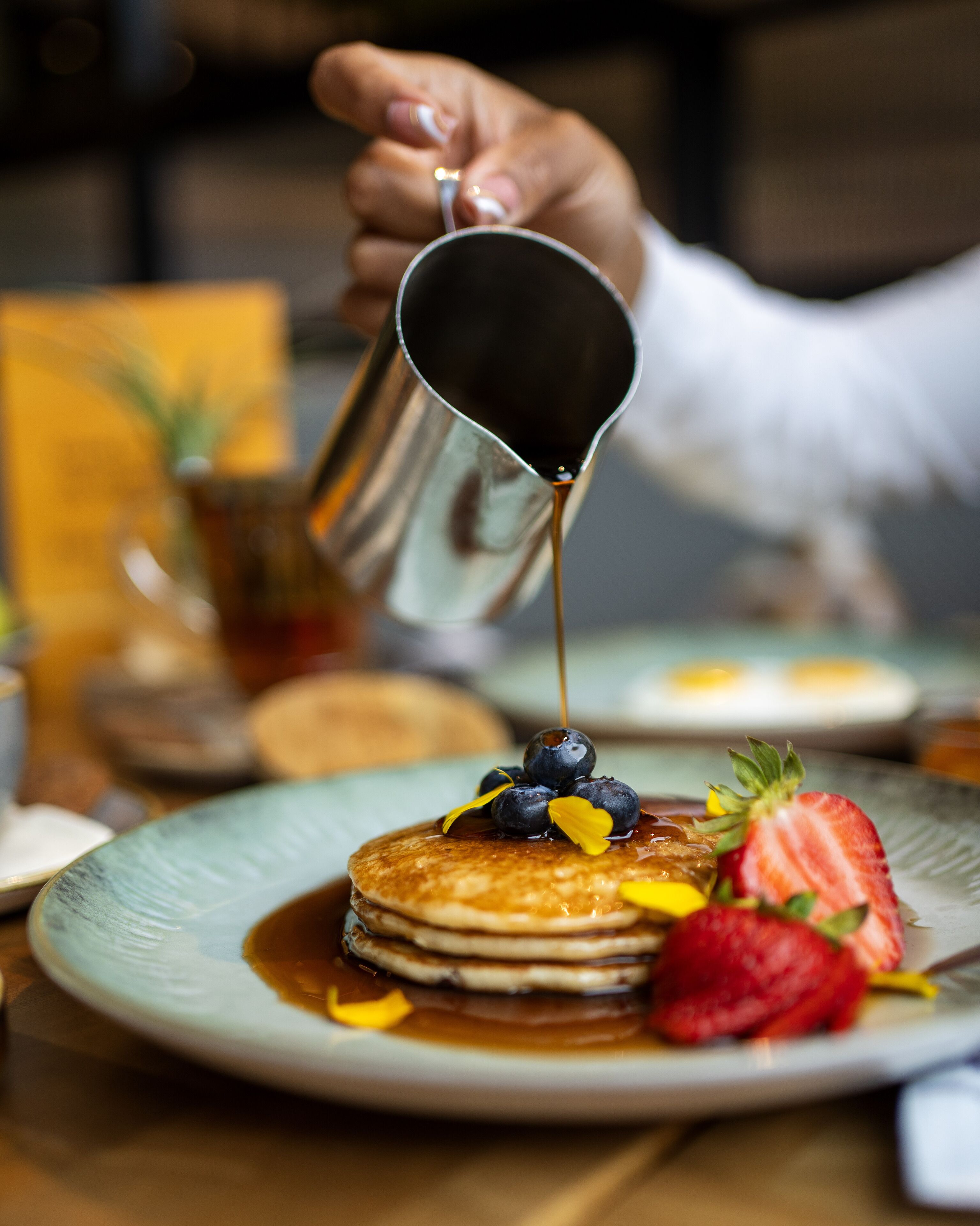 Ein Teller mit Pfannkuchen, Sirup, Blaubeeren und einer Erdbeere – Detailaufnahme.