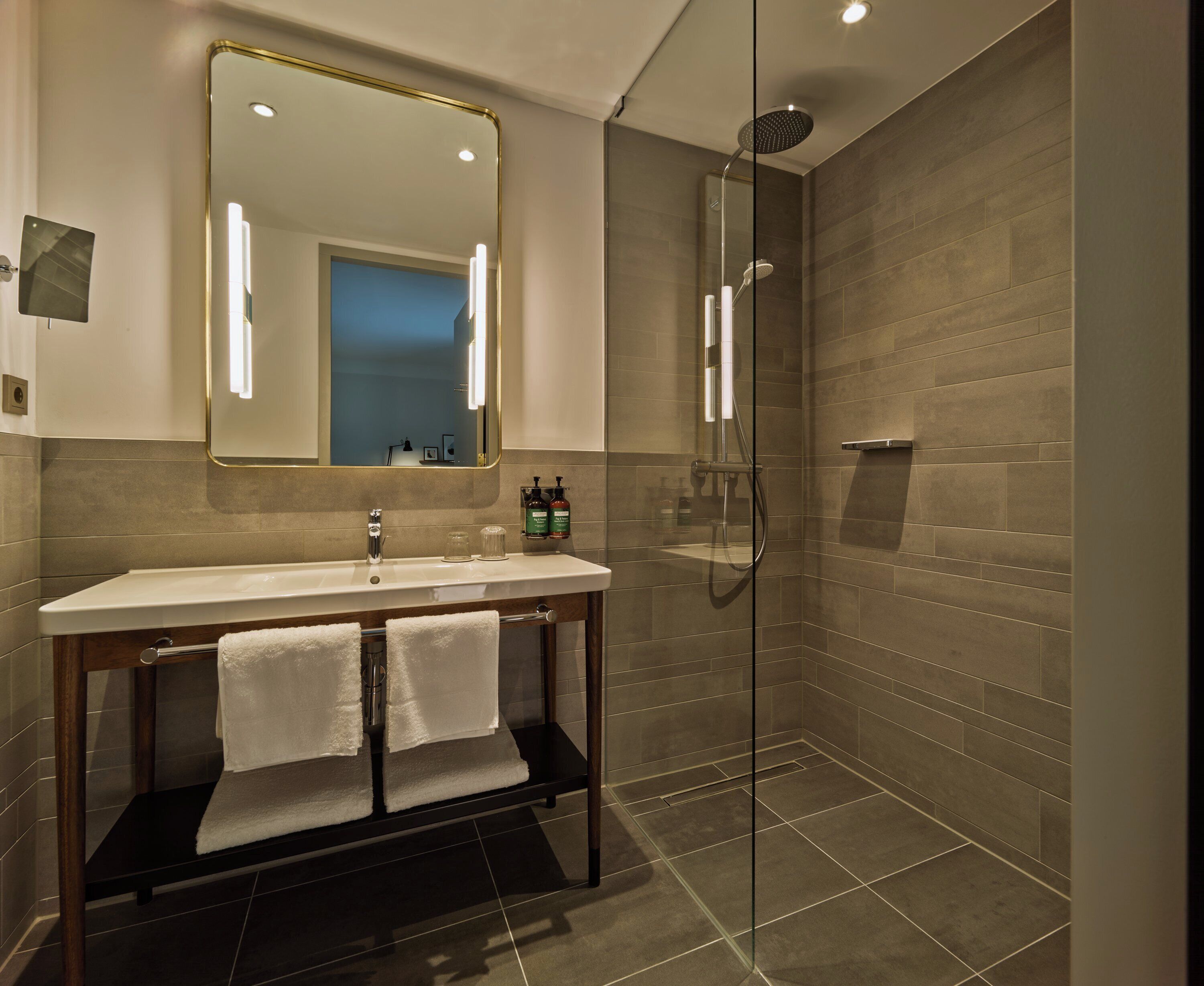 A modern bathroom with a glass-enclosed shower, a large mirror, and a vanity with a sink and towel rack.