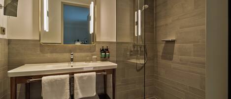 Un baño moderno con ducha de vidrio, un espejo grande y un tocador con lavamanos y barra para toallas.
