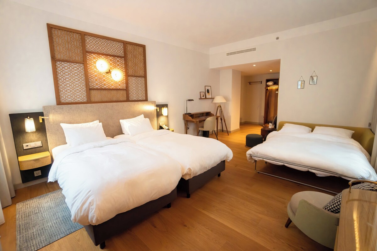 A hotel room with two beds, a desk, a chair, and a decorative wall panel.
