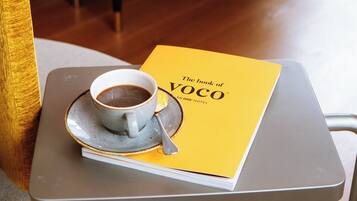 Un libro con el título "The book of VOCO" sobre una bandeja con una taza de café y una cuchara.
