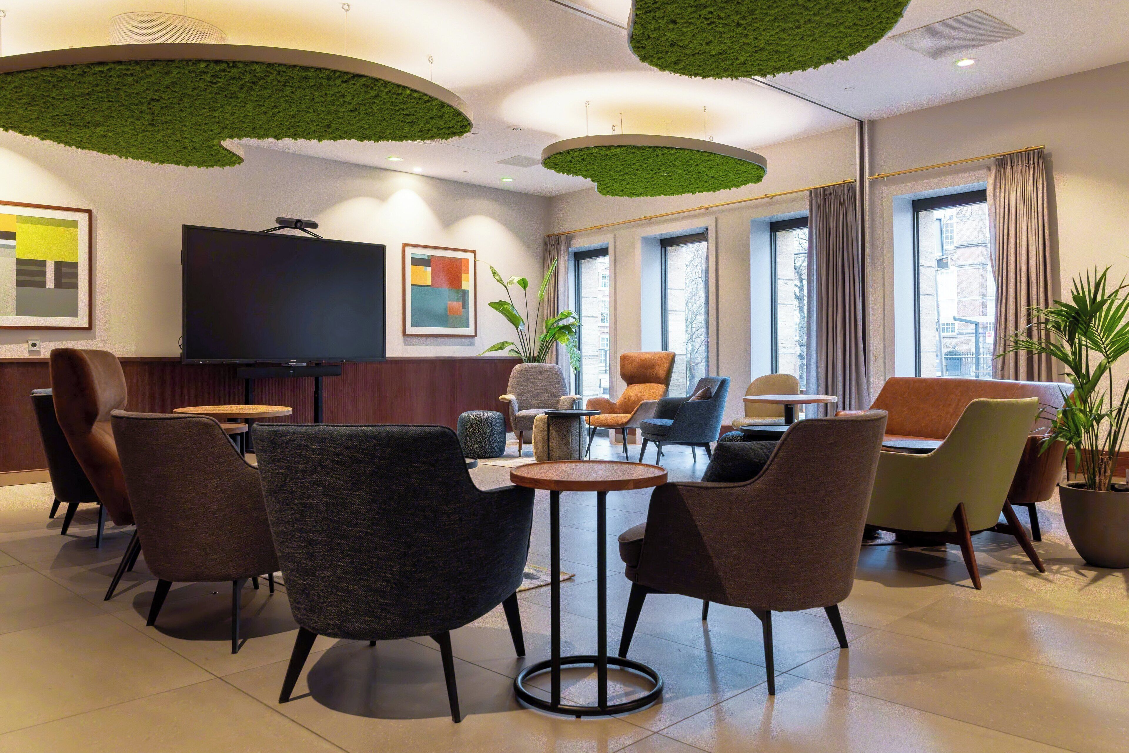 A modern hotel lobby with a flat-screen TV, comfortable seating, large windows, and a ceiling with green accents.