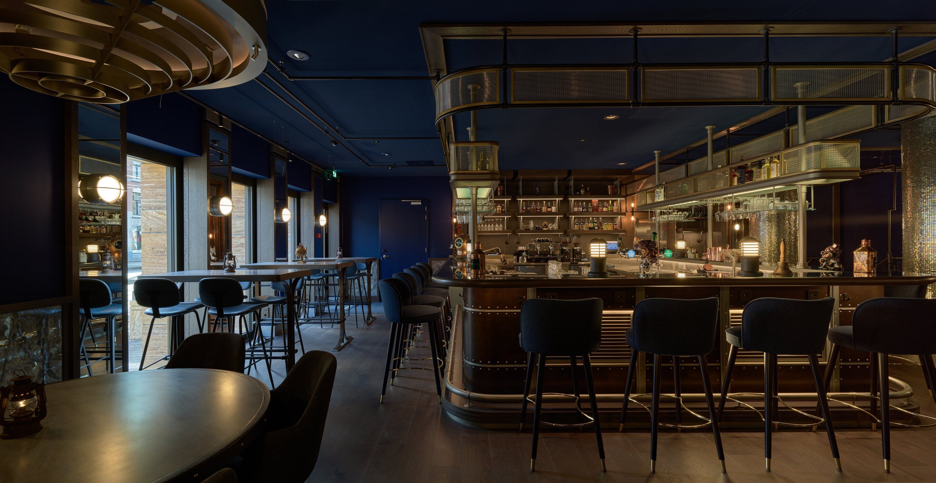 A modern bar area with a curved counter, bar stools, and a seating area with tables and chairs.