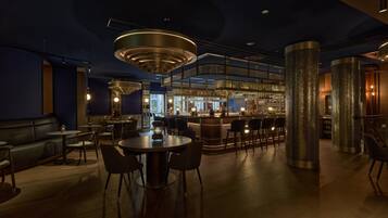 Uma área de bar moderna com um candelabro circular, disposições de assentos e um balcão.