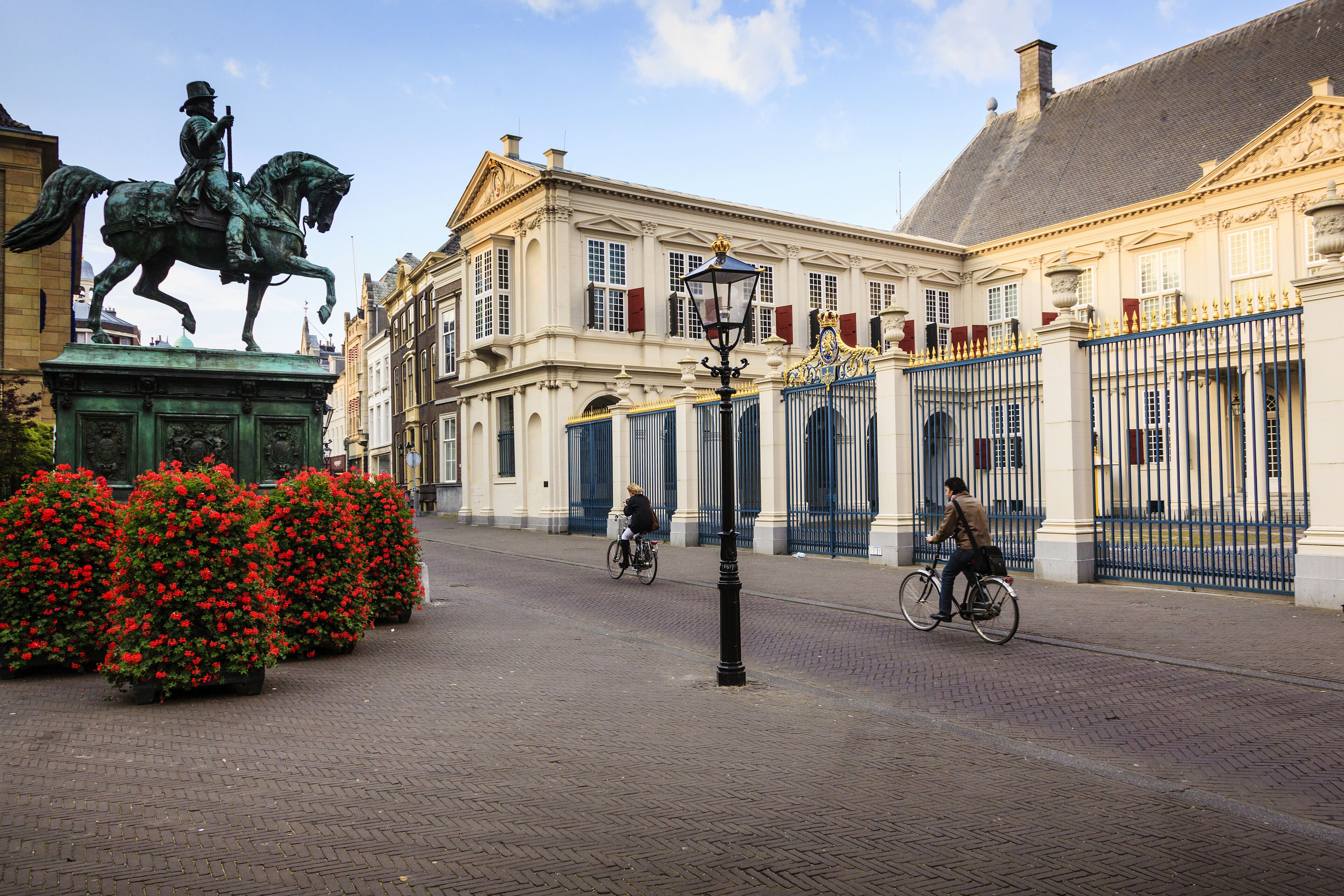 A cobblestone street with a statue of a man on a horse, red flowers, and a building with a blue gate.
