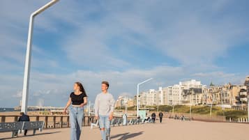 Un paseo marítimo con bancos, una noria y edificios al fondo.