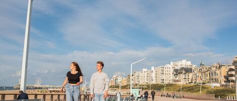 A promenade with benches, a Ferris wheel, and buildings in the background.