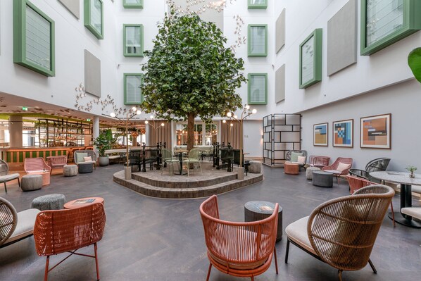 A spacious indoor area with a central tree, seating arrangements, and artwork on the walls.