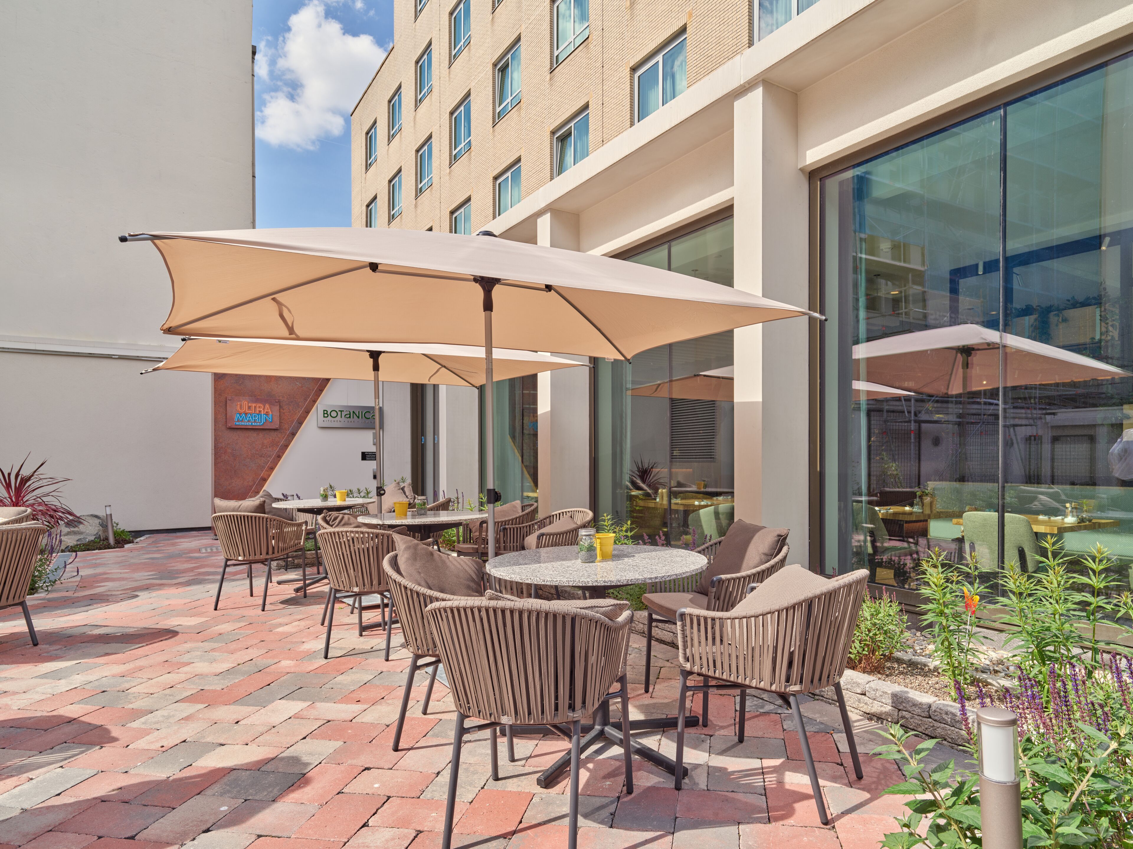 An outdoor patio area with wicker chairs and round tables, shaded by large umbrellas, and a sign for "Ultra Marín Botanica."