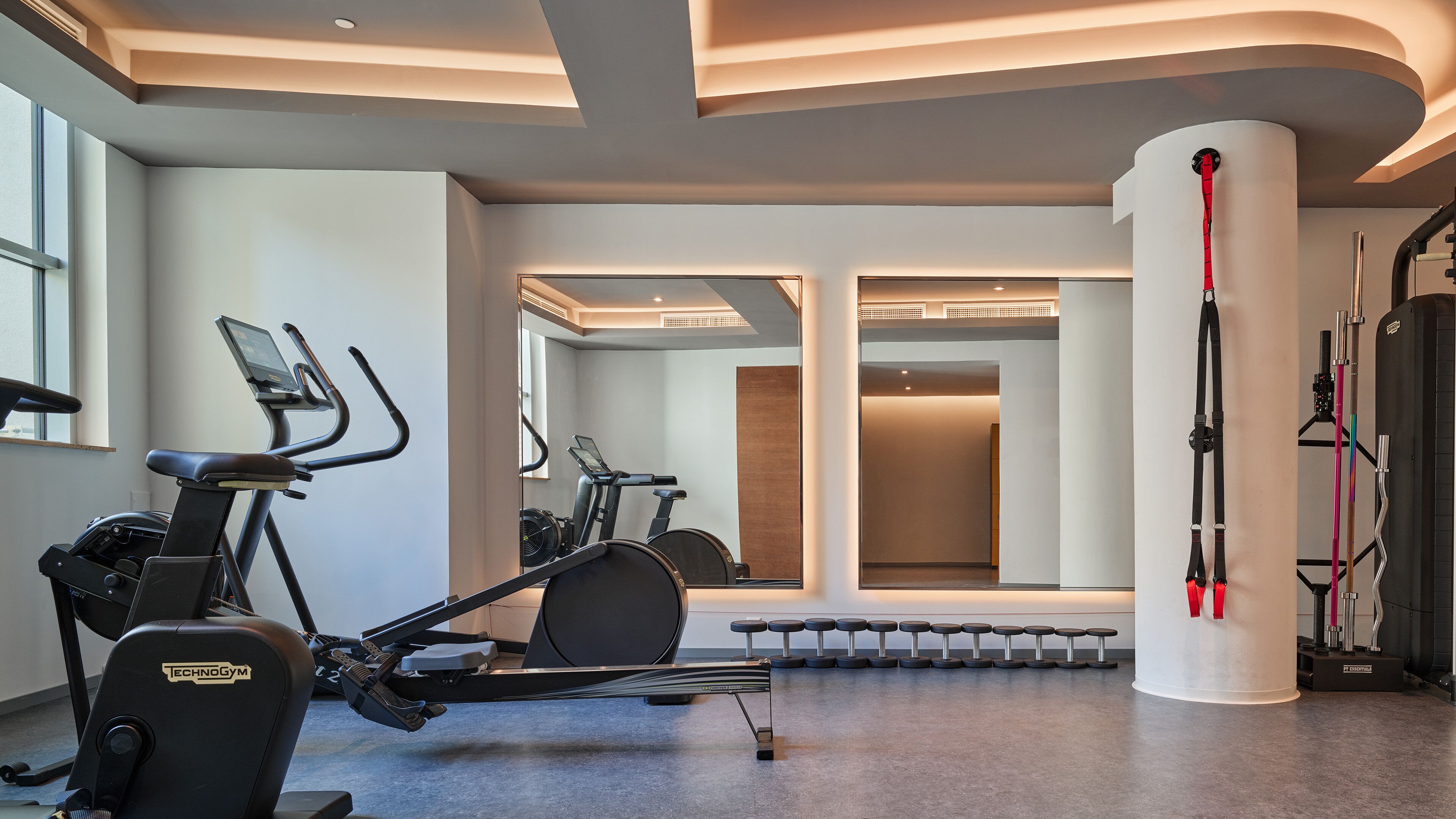 A modern gym with exercise equipment, large mirrors, and a minimalist design.