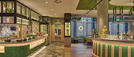 A modern restaurant with a curved counter, green-tiled bar area, and a ceiling with hanging lights.