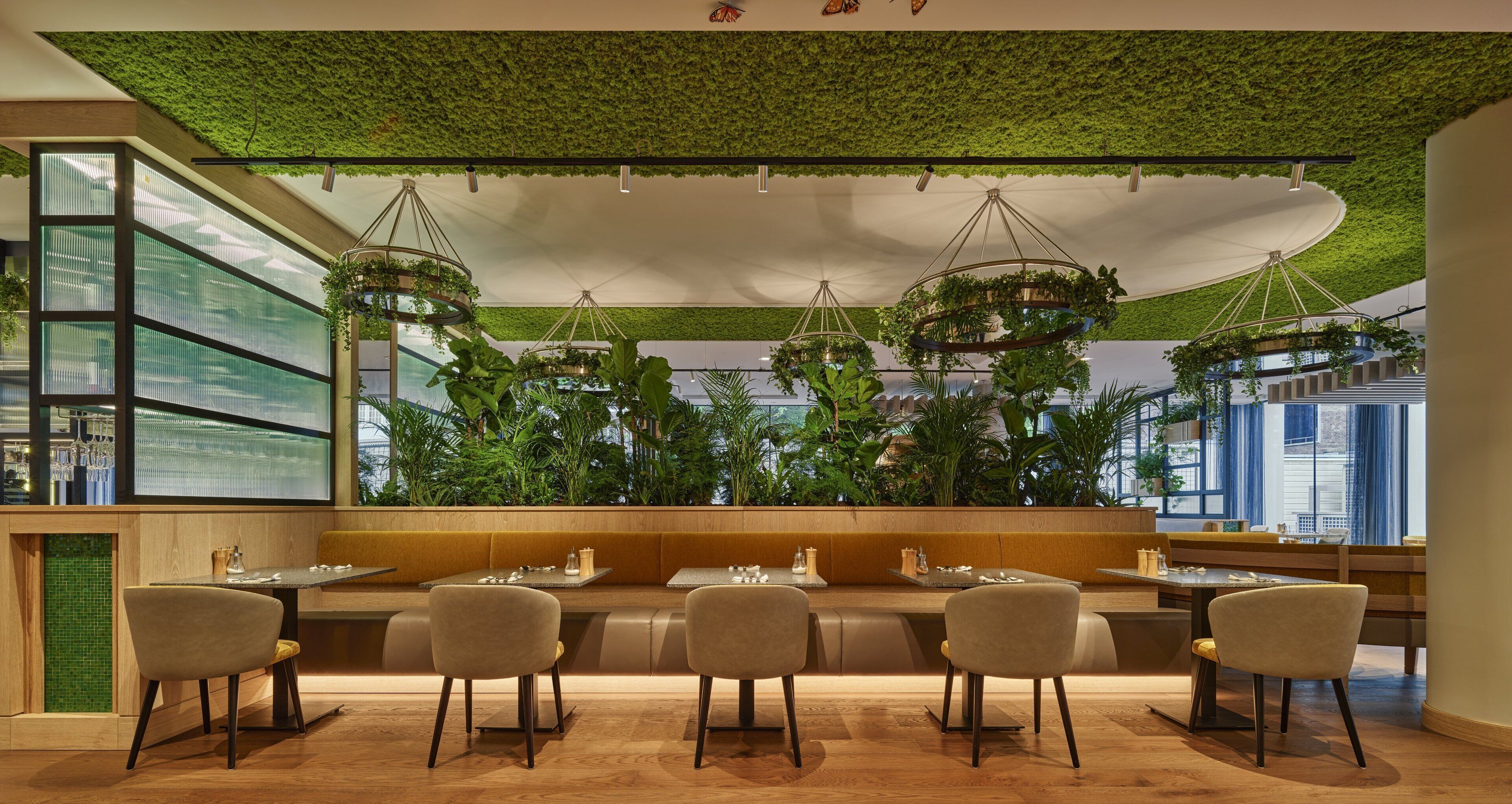 A restaurant with a green ceiling, hanging plants, and a modern seating arrangement.
