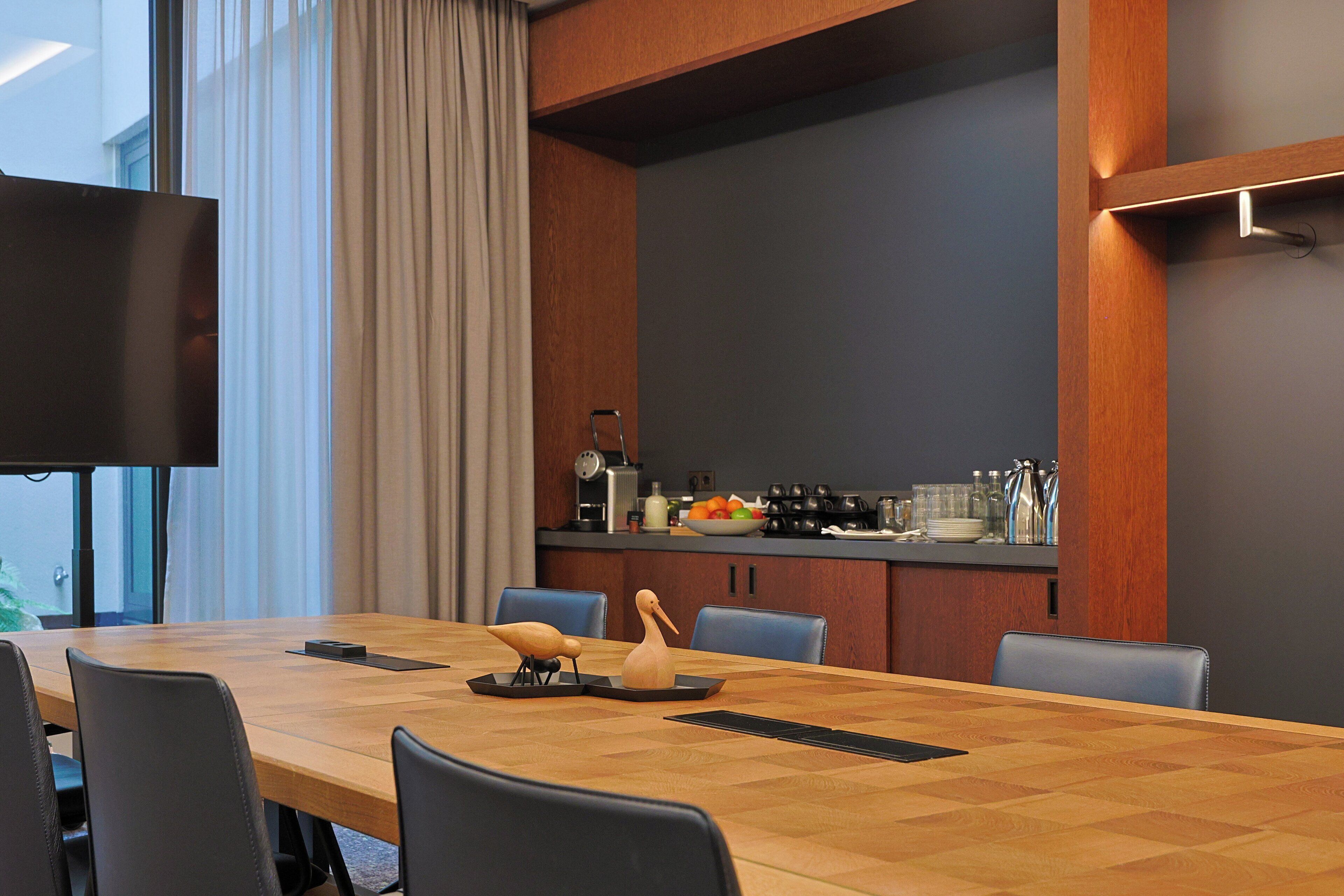 A modern conference room with a long wooden table, black chairs, and a flat-screen TV mounted on the wall.
