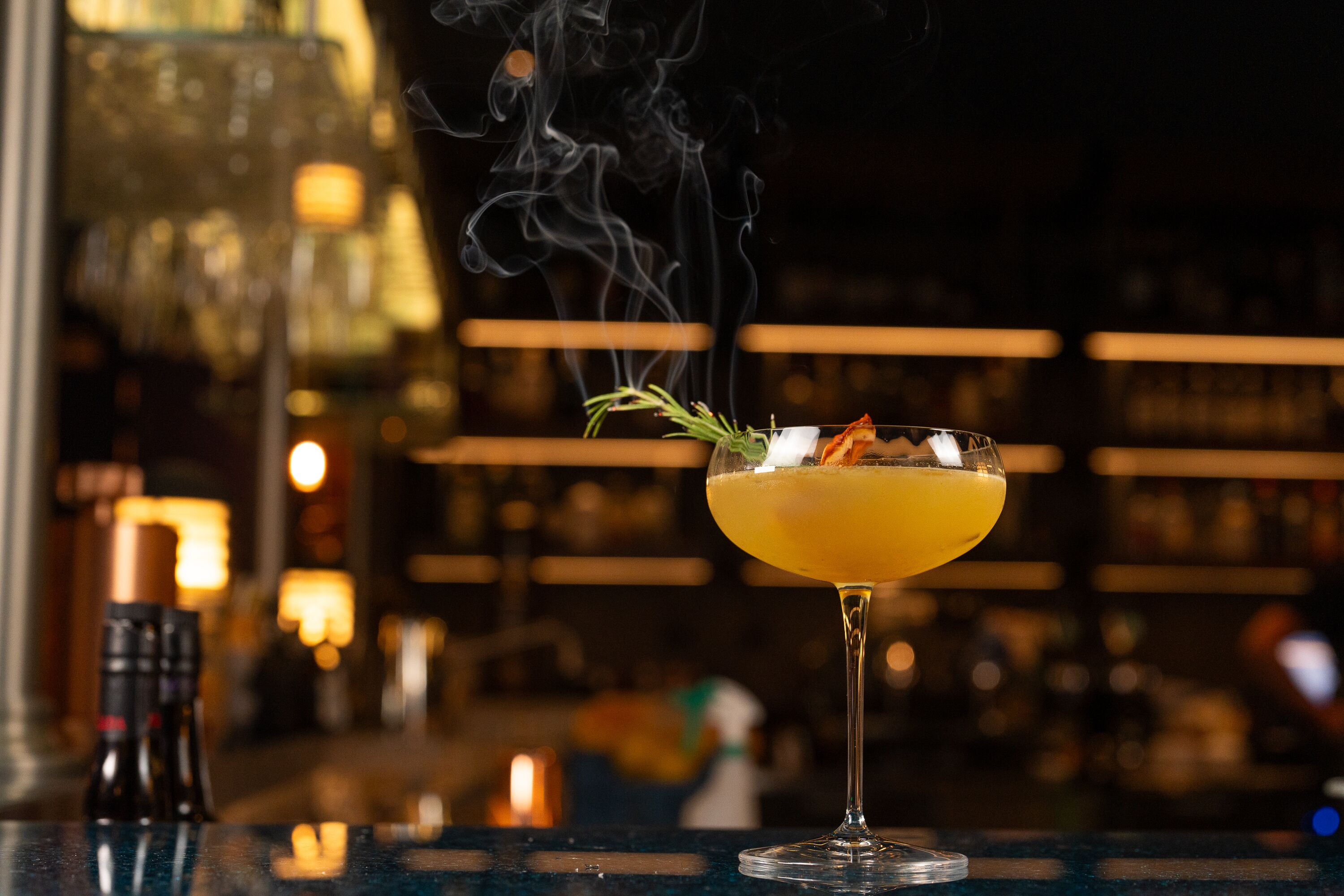 Een cocktail met rook, een glas en een bar op de achtergrond.