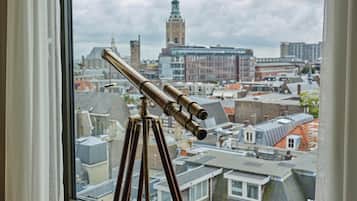 Un telescopio su un treppiede vicino a una finestra con vista su un paesaggio urbano, con edifici storici e una torre dell'orologio.