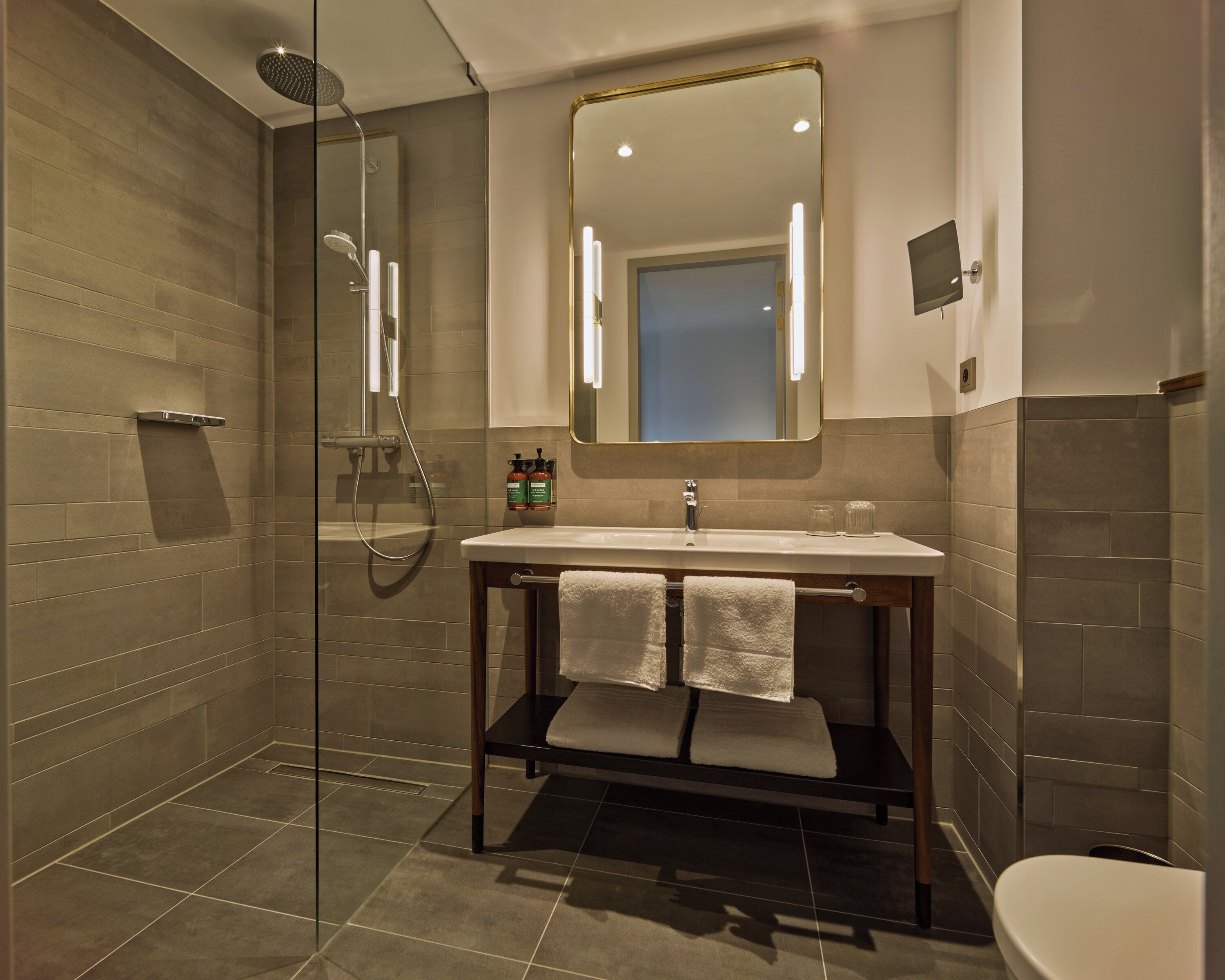 A modern bathroom with a glass-enclosed shower, a sink with a mirror above, and a toilet.