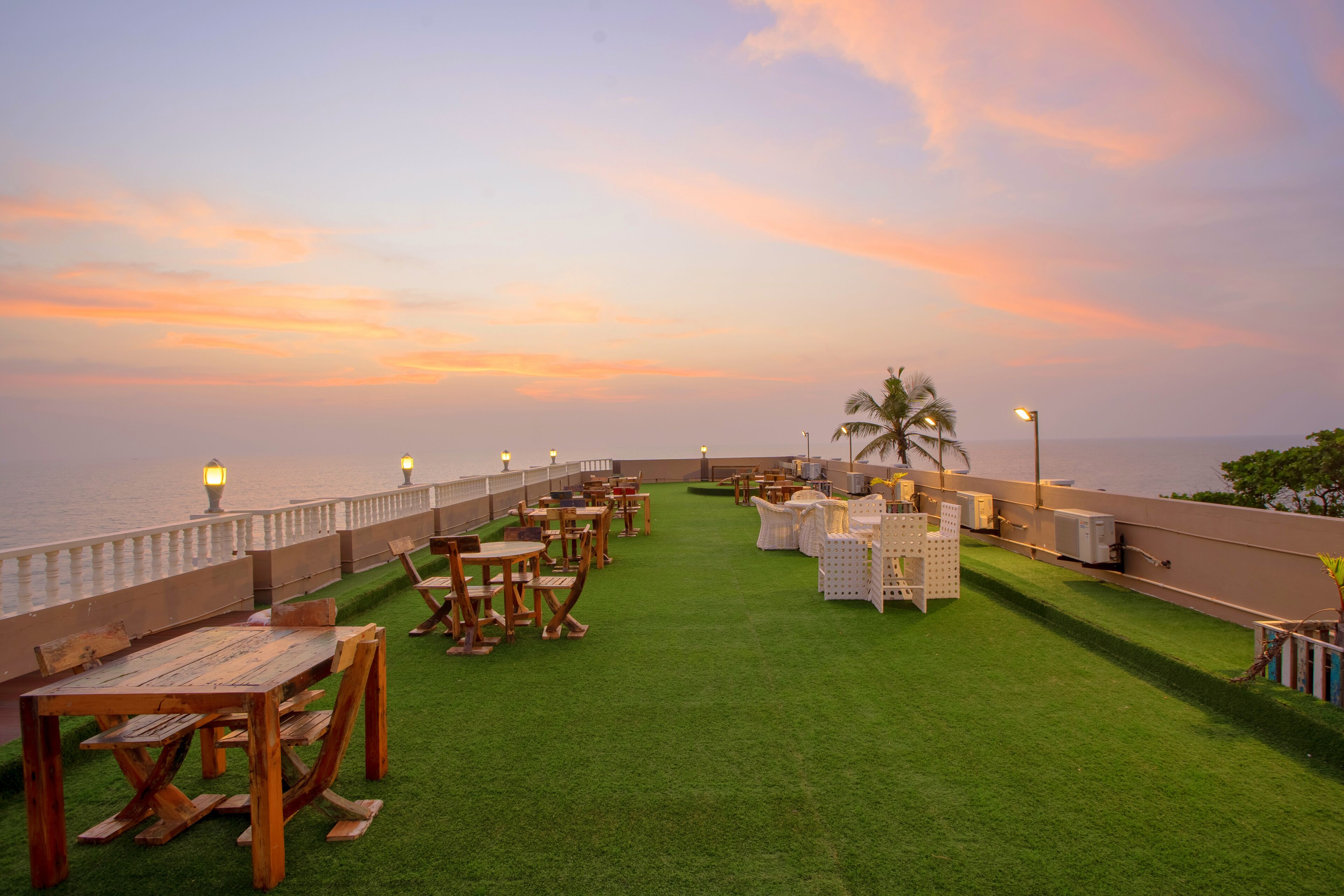 Una terraza en la azotea con mesas y sillas, barandilla y vista al mar.